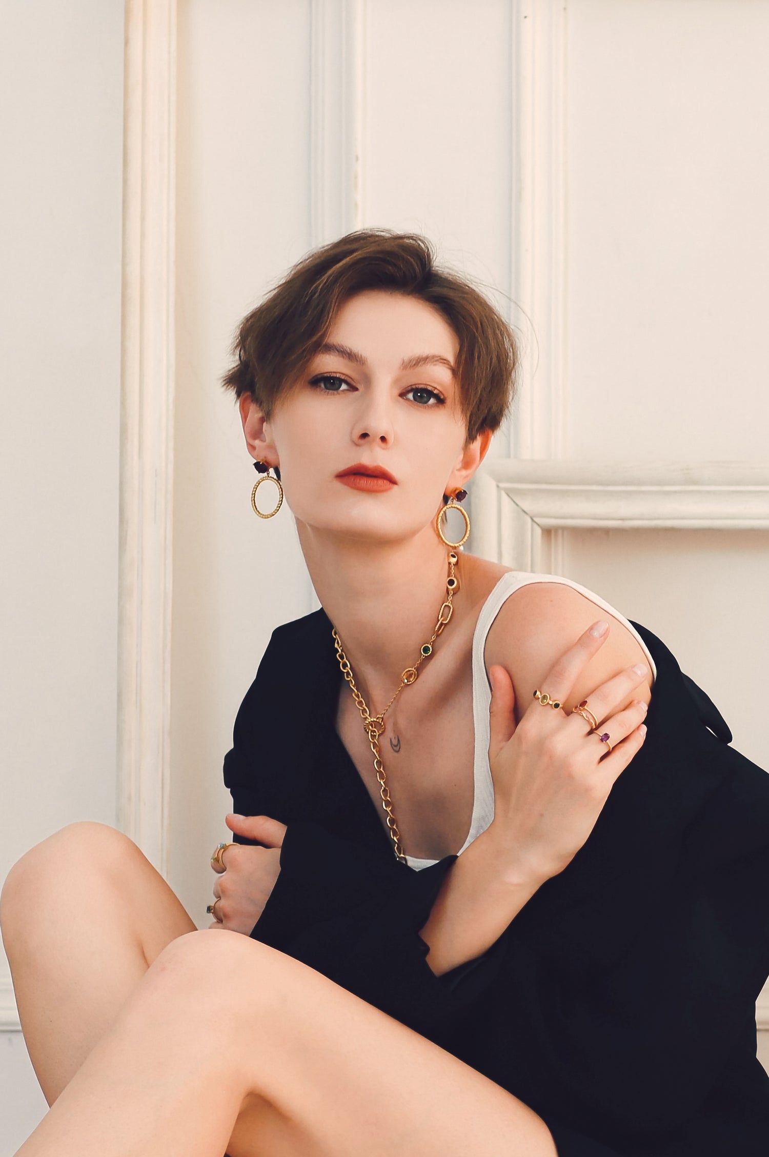 Short hair woman wearing black suit and vintage gold earrings, necklace and rings